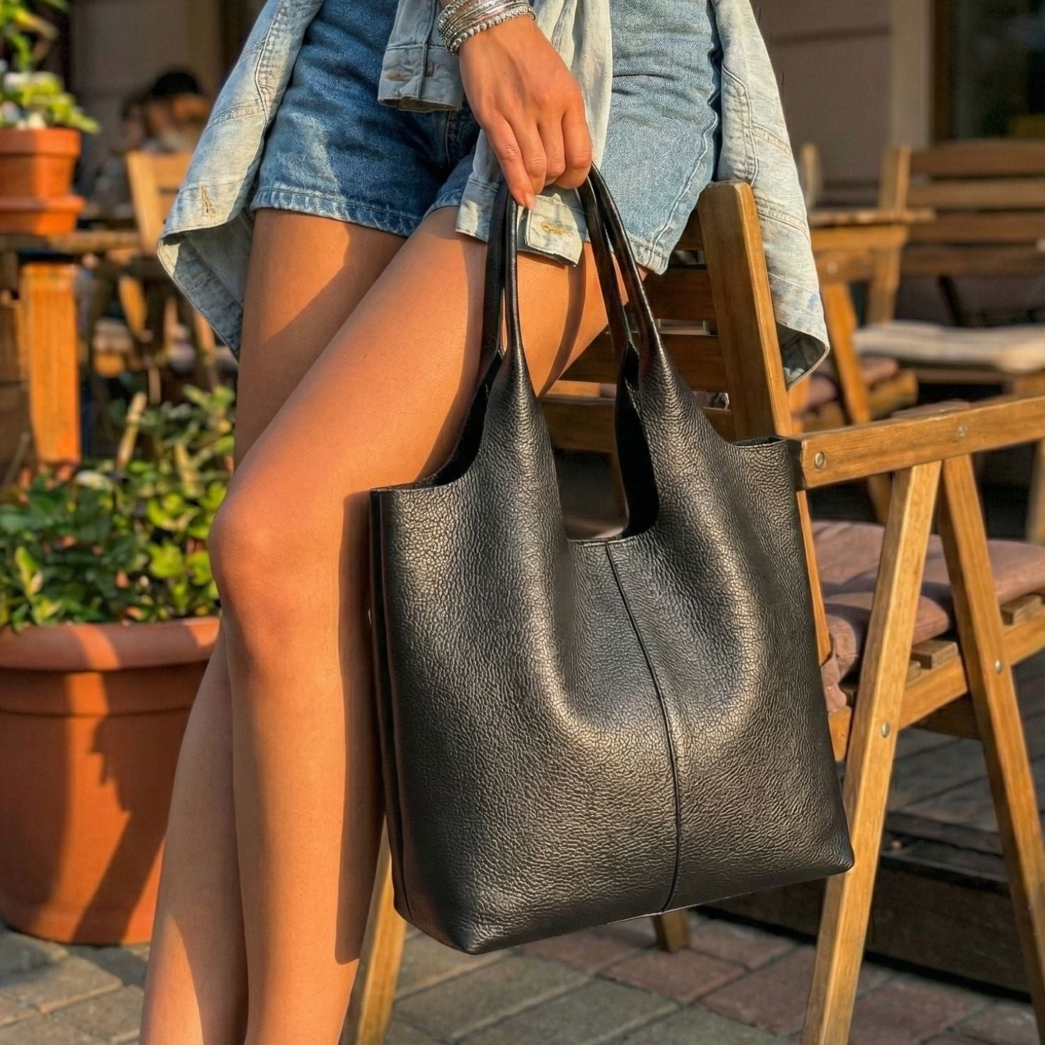 Bolso shopper de cuero negro formato vertical con costura central posado sobre silla de madera