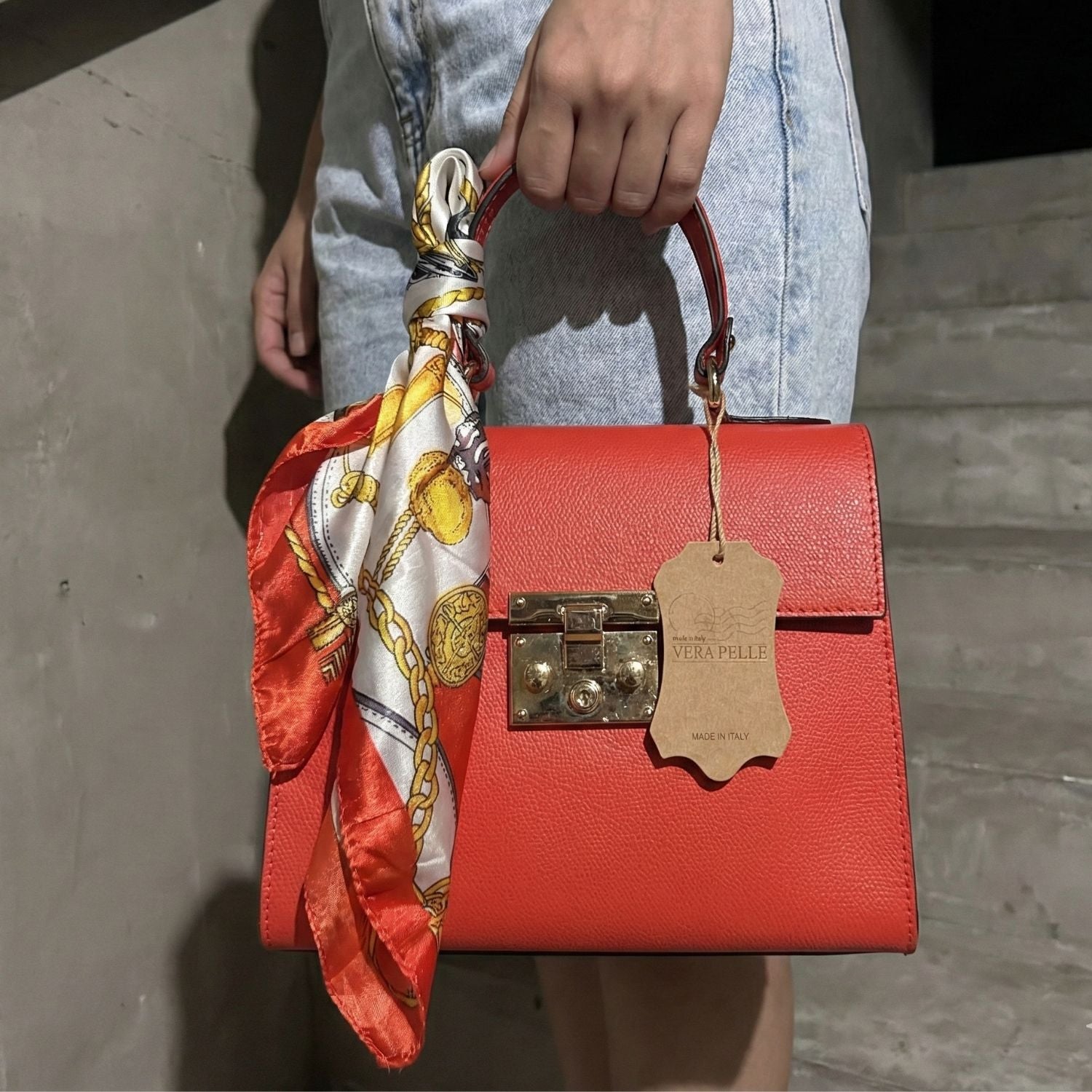 Detalle del asa y acabados dorados del mini tote de cuero rojo coral sostenido por la mano