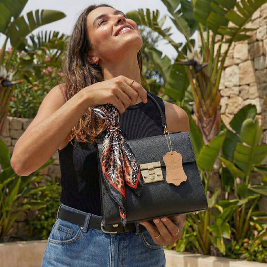 Mujer sonriendo sosteniendo bolso mini tote negro de cuero italiano con pañuelo elegante